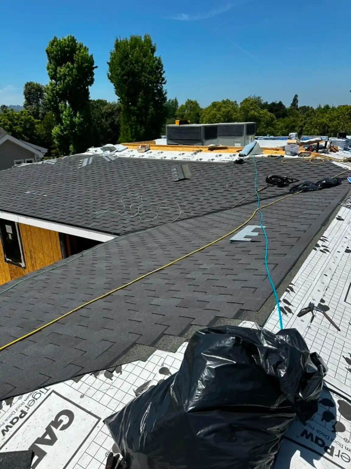 Roofing installation in progress with asphalt shingles, moisture barriers, and tools visible, showcasing a residential roofing project by Infinity Roofers.