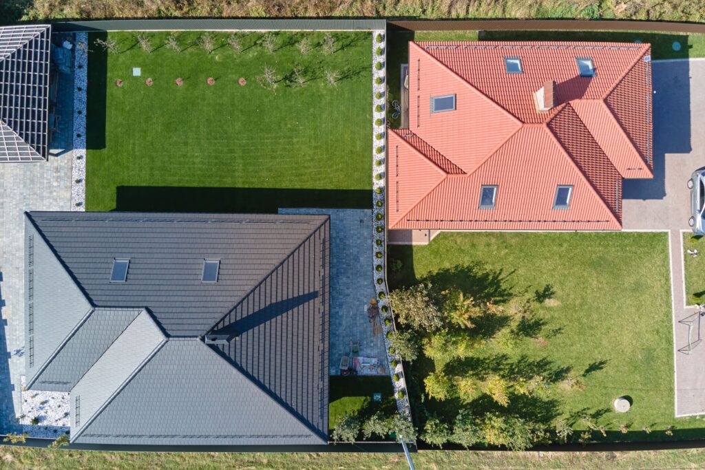 Aerial view of two homes in Simi Valley featuring energy-efficient roofing; one with dark solar-reflective shingles and the other with red clay tiles, surrounded by well-maintained lawns and landscaping.