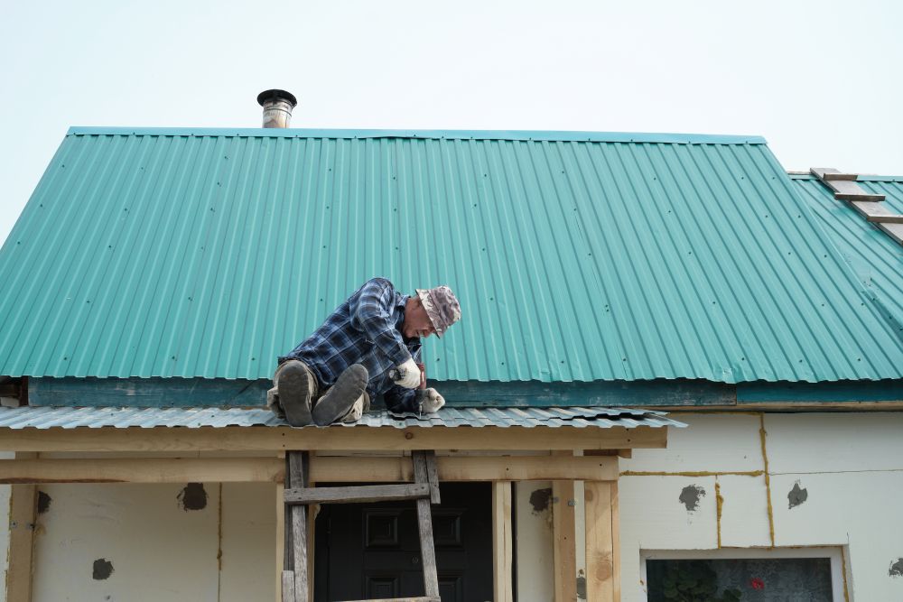 Man repairing a metal roof with green panels, demonstrating precise installation techniques, while using tools to secure the roofing materials.