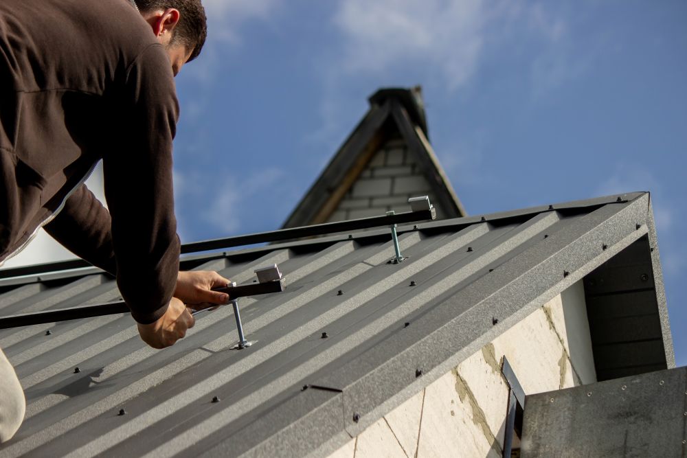 Man installing solar panel mounts on a metal roof, showcasing durable roofing material and professional craftsmanship.