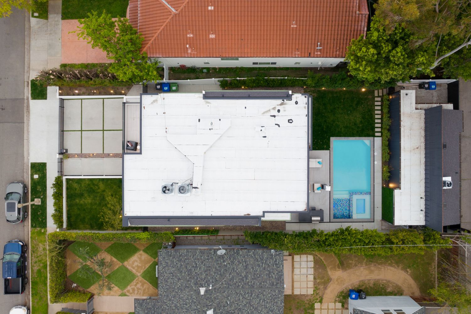 Aerial view of a flat roof with a white membrane, adjacent to a swimming pool and landscaped yard, showcasing modern residential architecture and outdoor space.