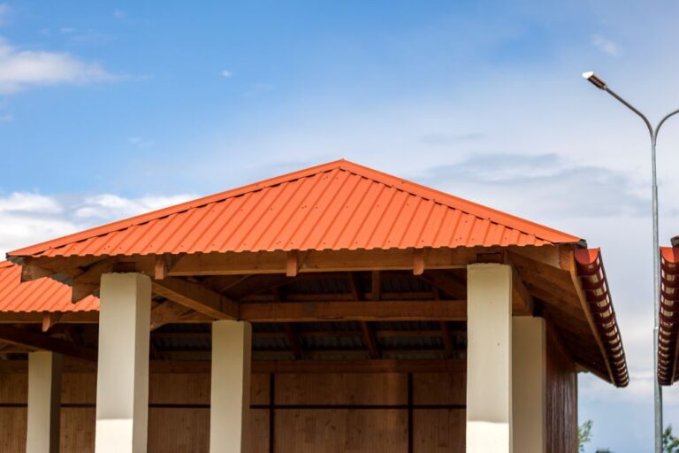 Metal roof with a vibrant red finish atop a wooden structure, showcasing modern design elements against a clear blue sky.