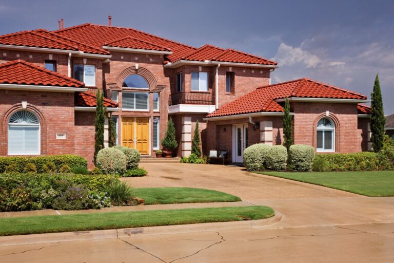 Tuscan-style home with red tile roof, brick exterior, and lush landscaping, showcasing the elegance and durability of tile roofing.