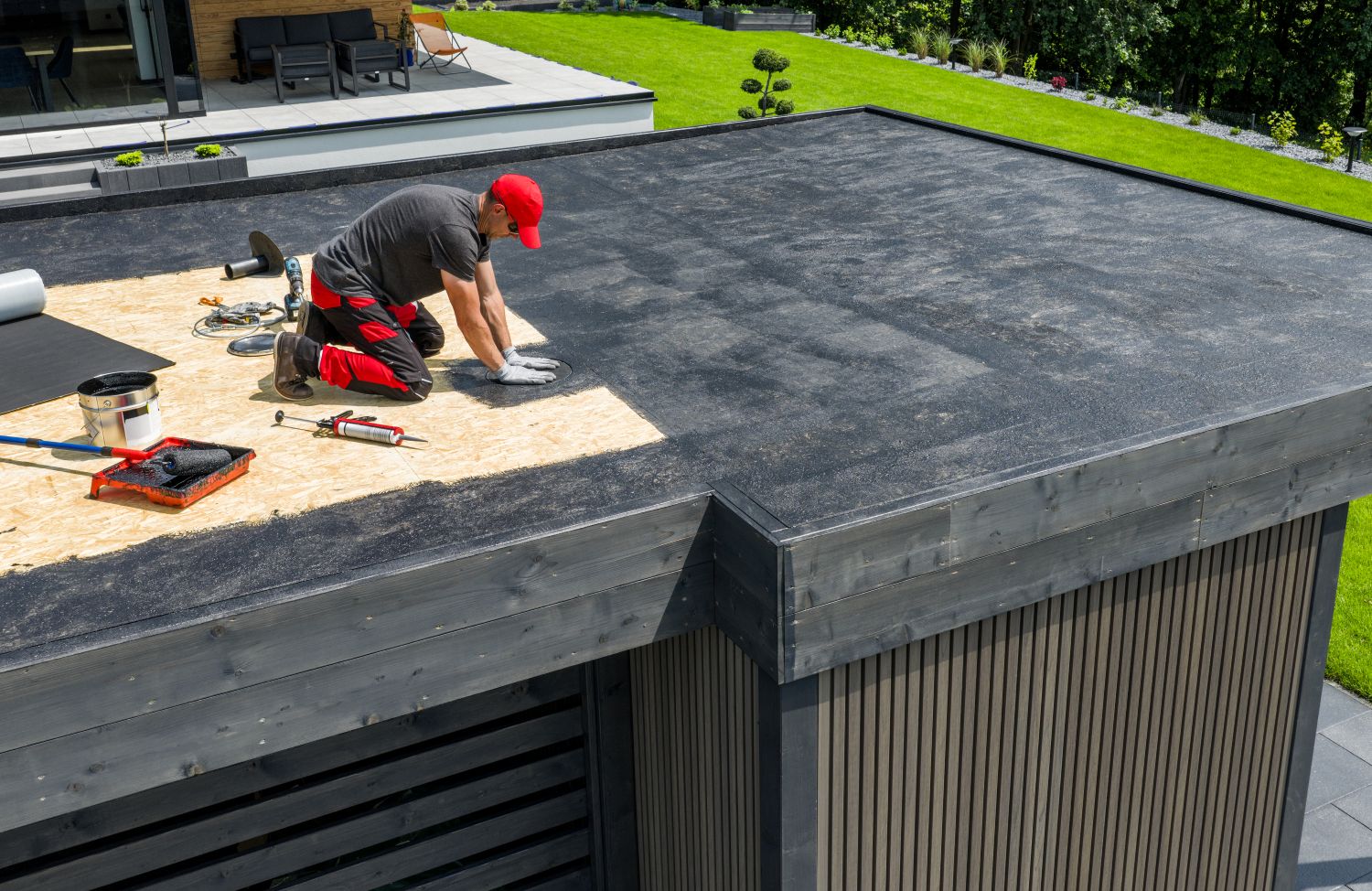 Worker installing EPDM roofing material on a flat roof with tools and materials, emphasizing modern roofing techniques for residential and commercial buildings.
