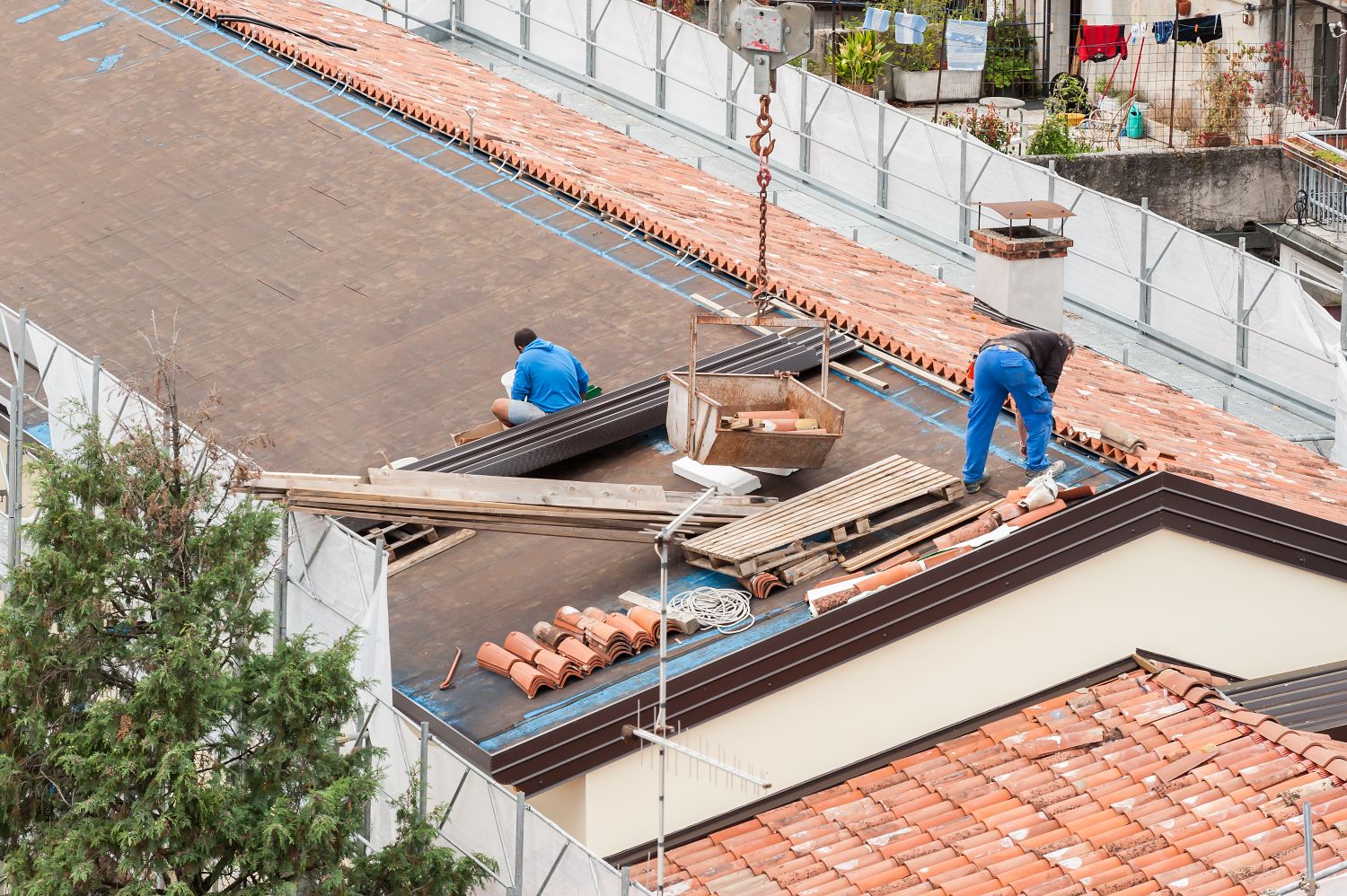 Workers installing tile roofing on a residential building, showcasing a mix of clay tiles and construction materials, emphasizing the roof installation process.