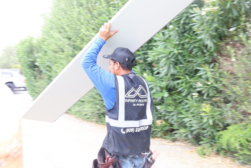 Infinity Roofers roofer carrying a standing seam metal roof panel on a Malibu job